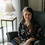 Brunette woman sitting comfortably in an armchair, enjoying a book in a cozy, well-lit living room.