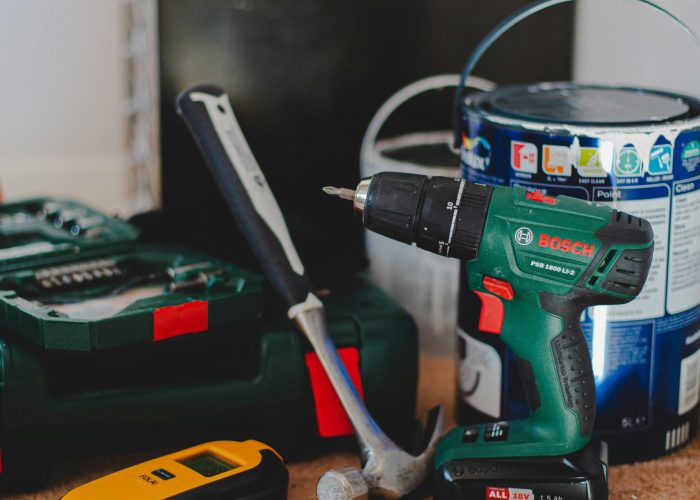 A selection of essential tools for home improvement projects, featuring a drill, hammer, and paint supplies.